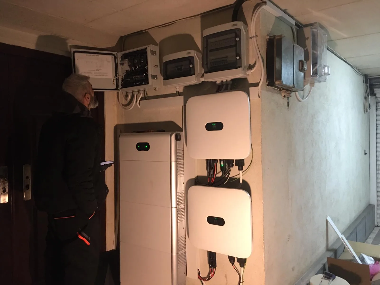 Un coleg verifică tabloul electric, lângă o baterie Huawei și două invertoare montate unul sub altul