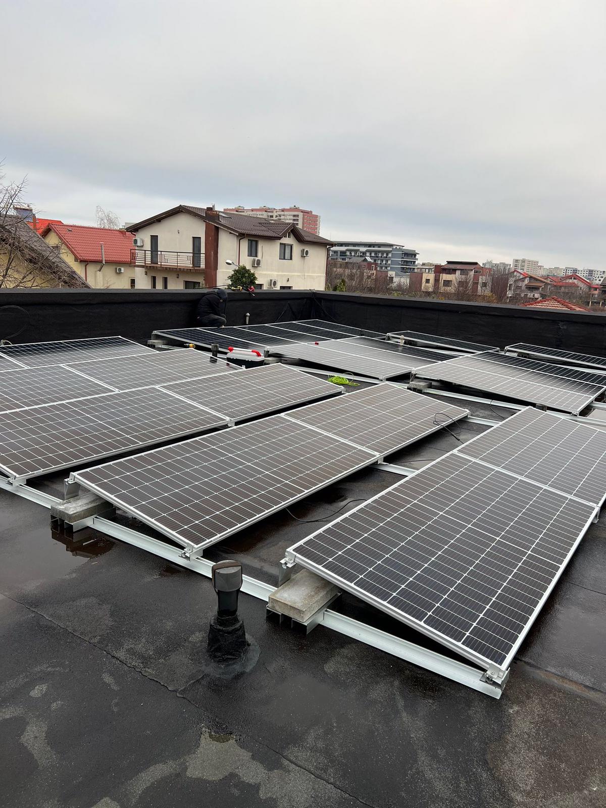 Panouri fotovoltaice pe un acoperiș-terasă, cu blocuri în fundal